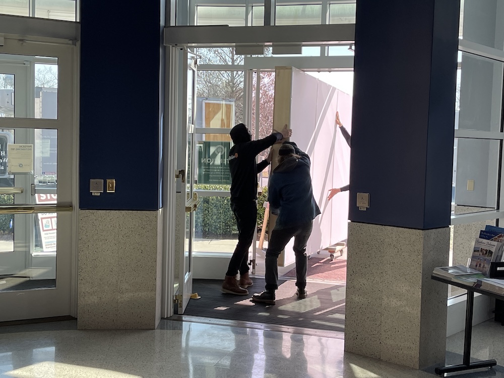 Two people carry The Crusaders through the glass doors in the Archives lobby.