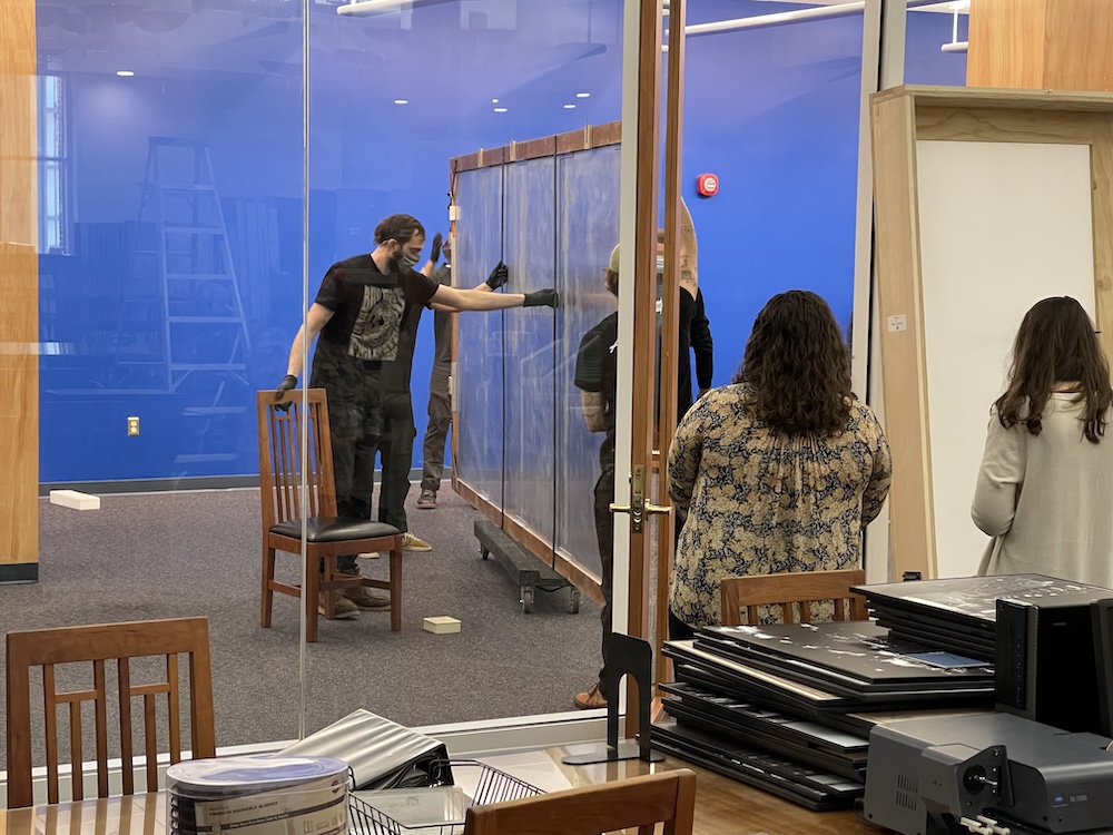 People in masks move The Crusaders through the Self-Service Microfilm Reading Room for placement on a vivid blue wall as others observe.