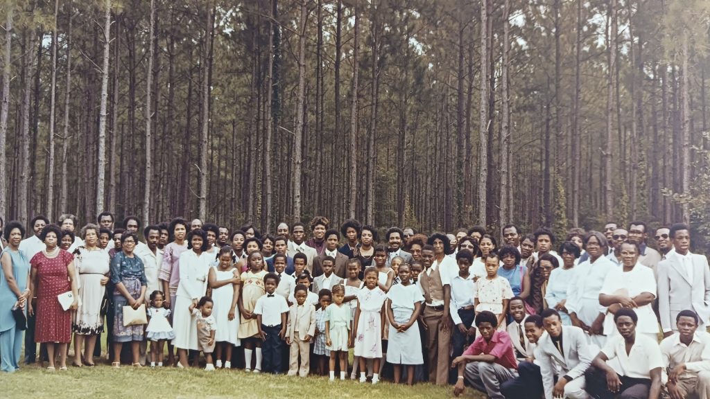 Wallace Green's family reunion in Georgia, from 9200-G13-001. A large group of people poses together for a photo in front of a forest.