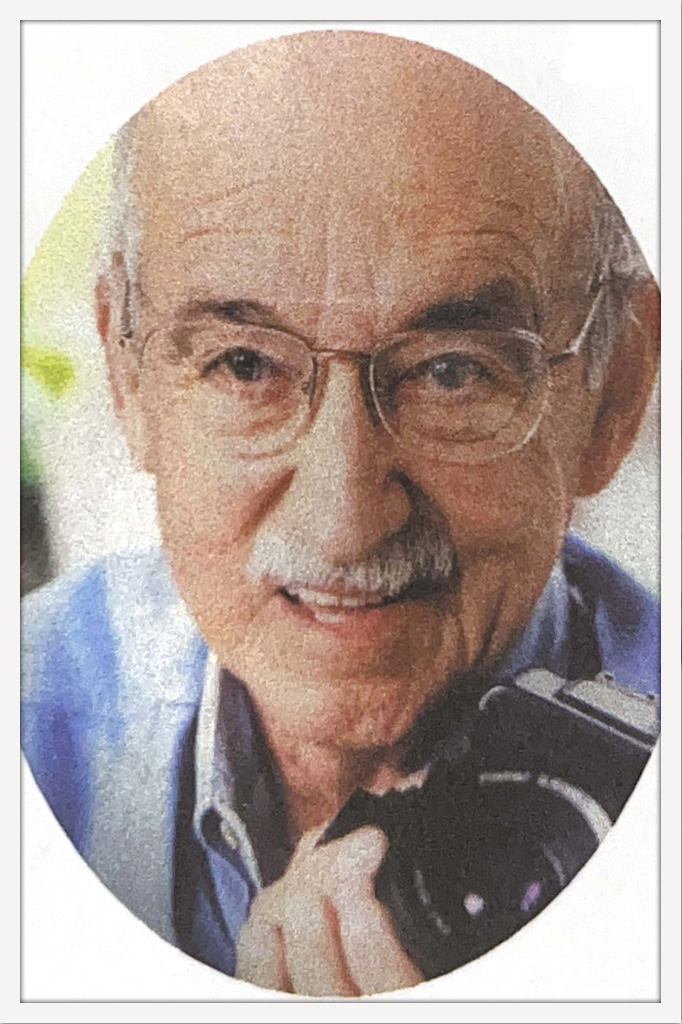 Oval portrait of an older Robert J. Bennett smiling while holding a camera.