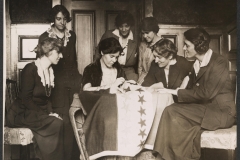 The National Woman’s Party activists watch as Alice Paul sews a start onto the NWP Ratification flag, representing another state’s ratification of the 19th Amendment.